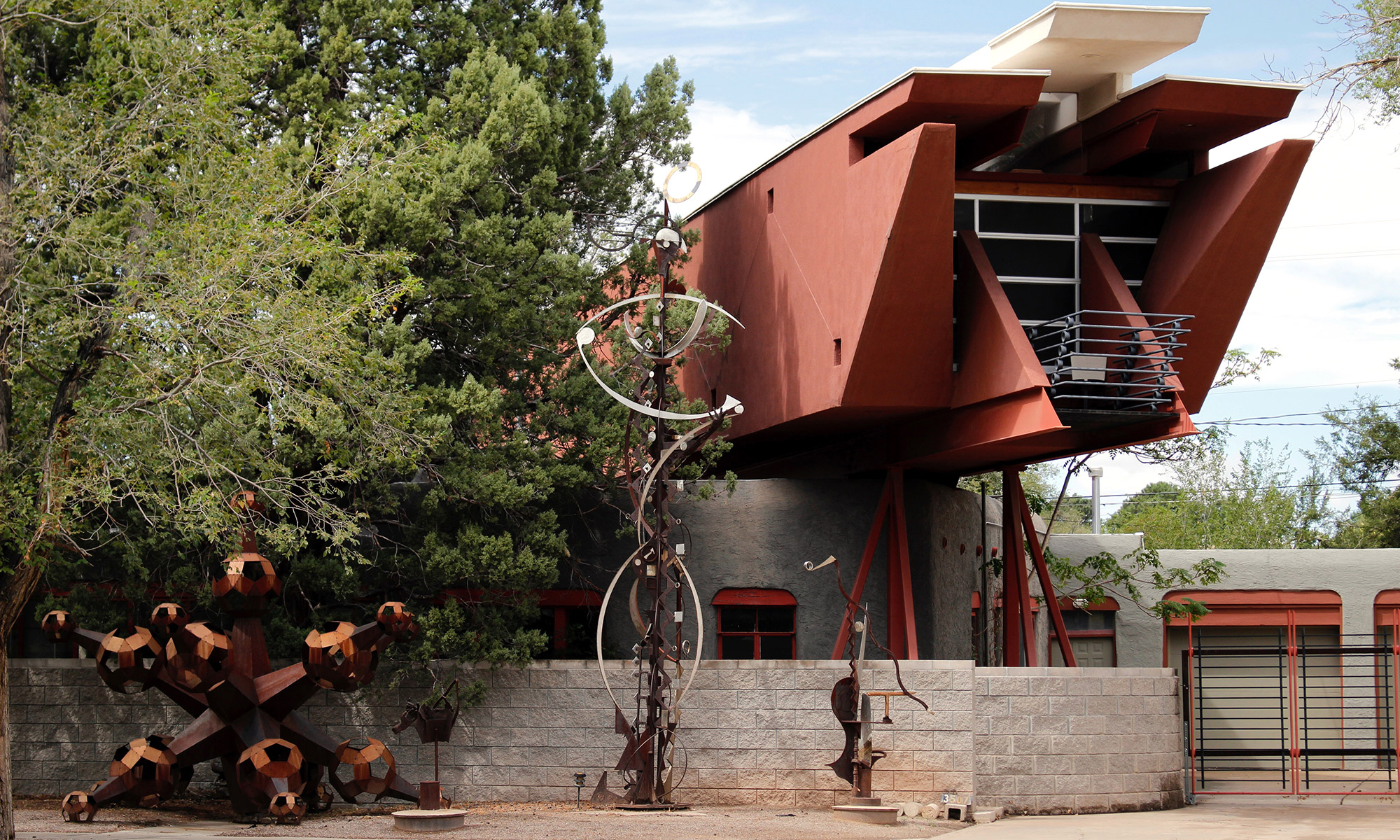 A red stucco home on stilts floating over another, smaller, gray stucco home in Albuquerque