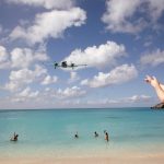 People swimming in the ocean, pointing up at an airplane flying overhead at Maho Beach in Sint Maarten