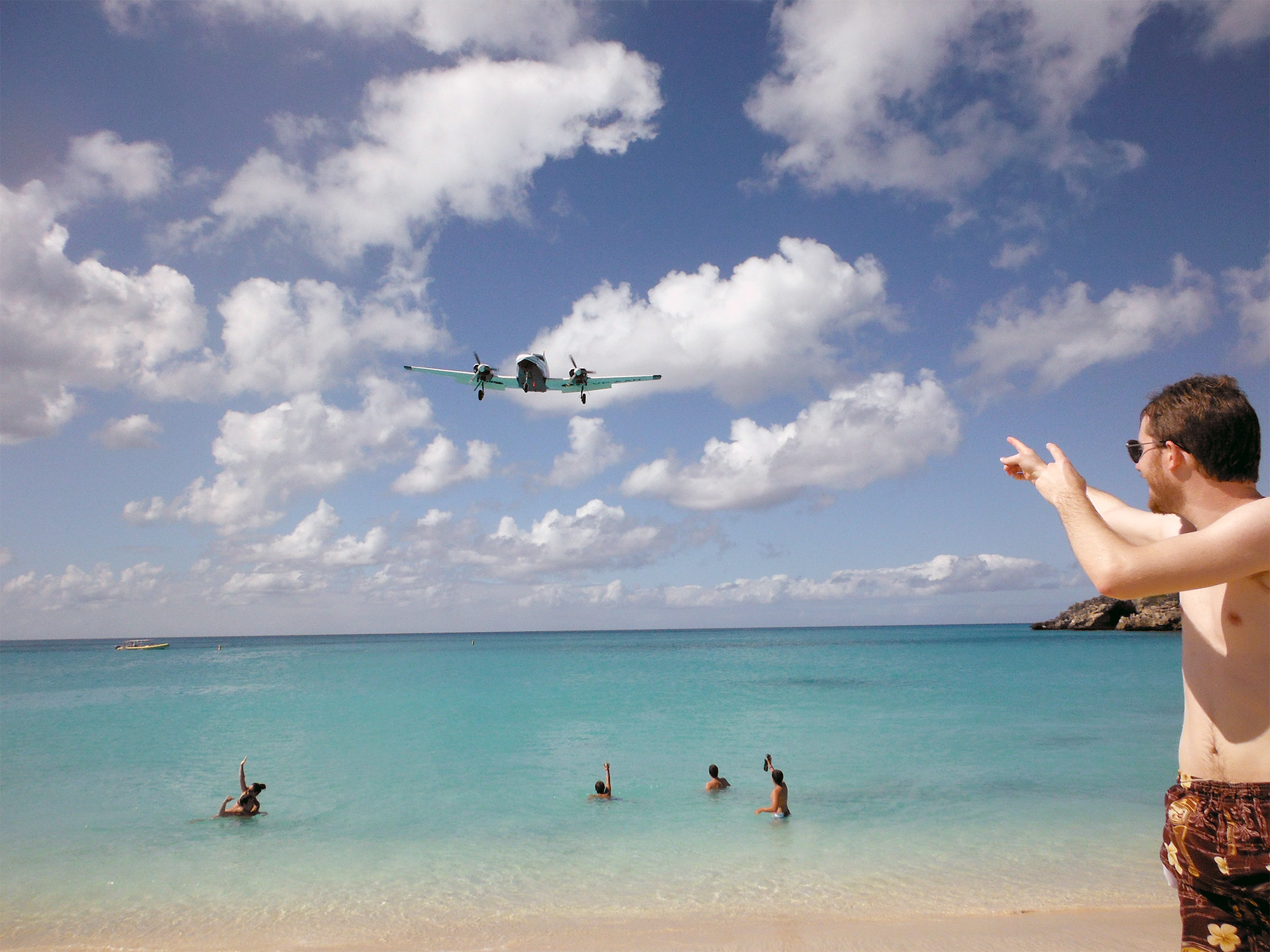 People swimming in the ocean, pointing up at an airplane flying overhead at Maho Beach in Sint Maarten