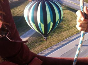 A hot air balloon prepares to land on the ground next to a highway overpass