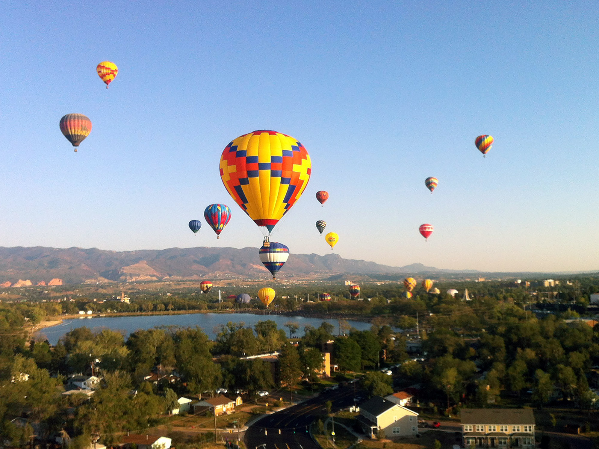 Dozens of hot air balloons taking off in the morning next to a lake with mountains in the background
