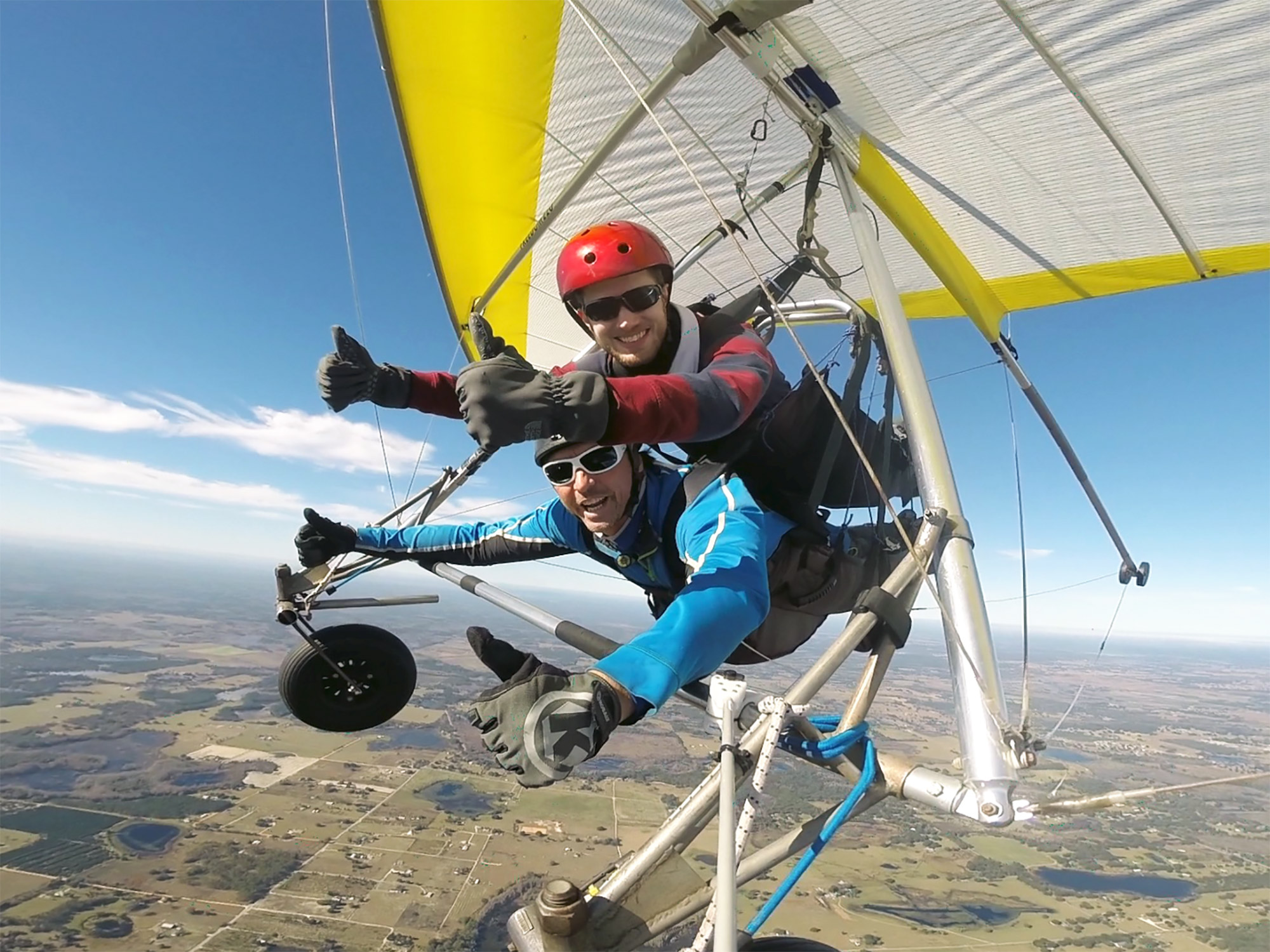 Ron Stauffer flying in a hang glider, smiling and holding two thumbs up.