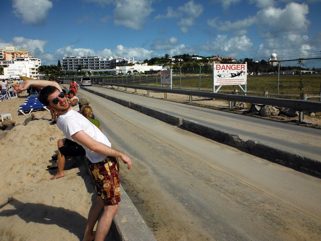 Ron Stauffer standing across the street from an airport runway in Sint Maarten by warning sign that says "danger"